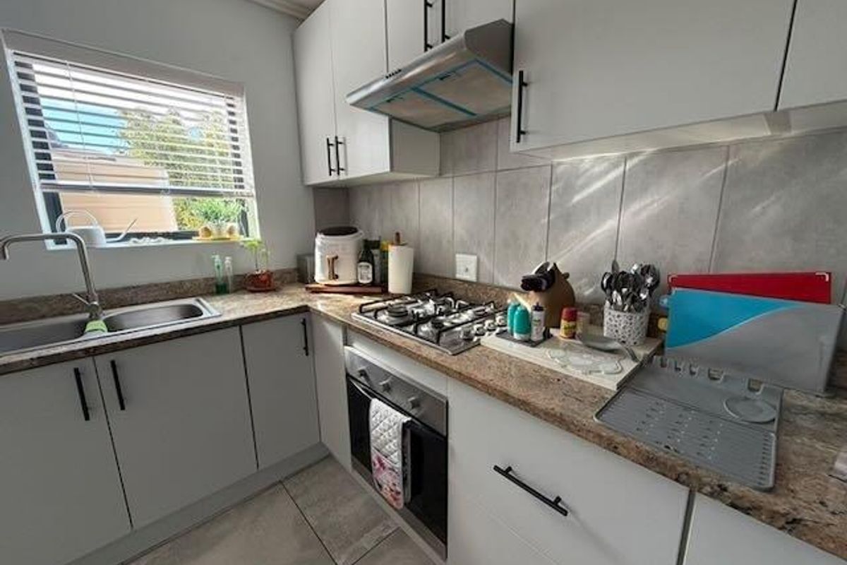 Modern kitchen featuring granite countertops, built-in cabinetry, gas hob, oven, extractor fan, and a stainless steel sink with a window view.