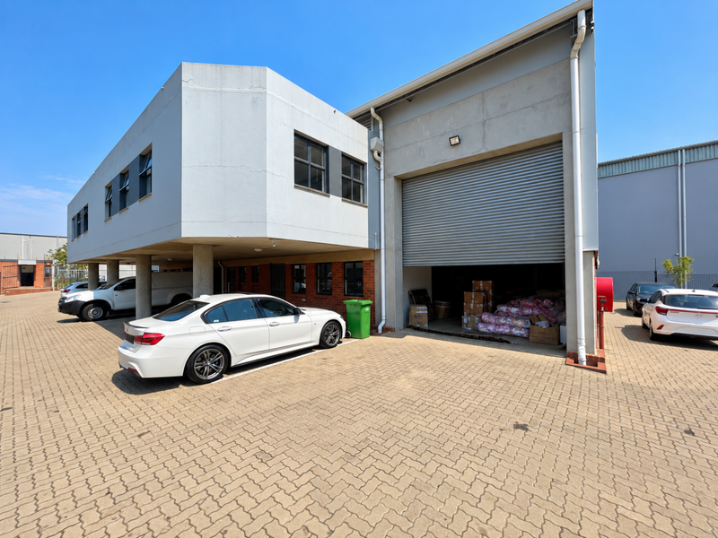 Front elevation of a mixed-use industrial building featuring a large roller shutter door, paved parking area, and concrete structural columns.