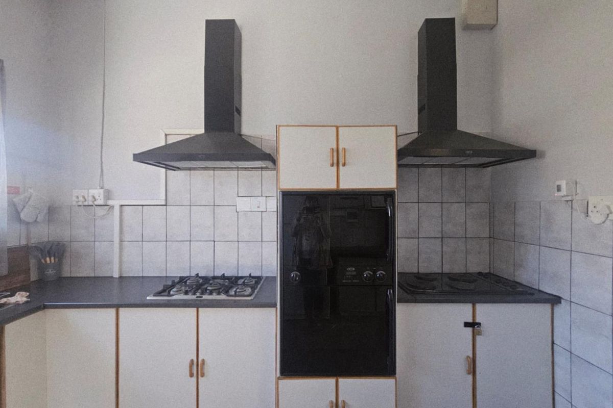 A functional kitchen area featuring dual extractor fans, built-in oven, gas hob, electric hob, and tiled splashbacks with ample storage cabinetry.