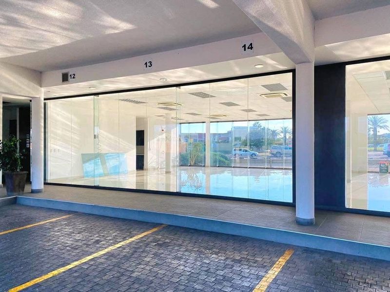Modern retail storefront with large glass display windows, tiled entrance walkway, and dedicated paved parking bays in front.