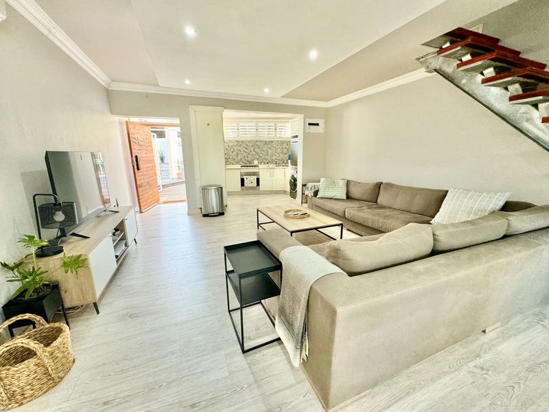 Open-plan living area featuring modern laminate flooring, recessed lighting, and a functional kitchen with built-in cabinetry and appliances, leading to an outdoor entrance.