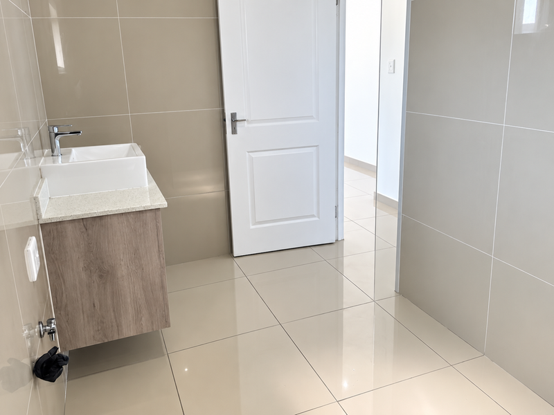 A modern, minimalist bathroom featuring a wall-mounted vanity with a vessel sink, stone countertop, and neutral large-format ceramic tiling throughout.