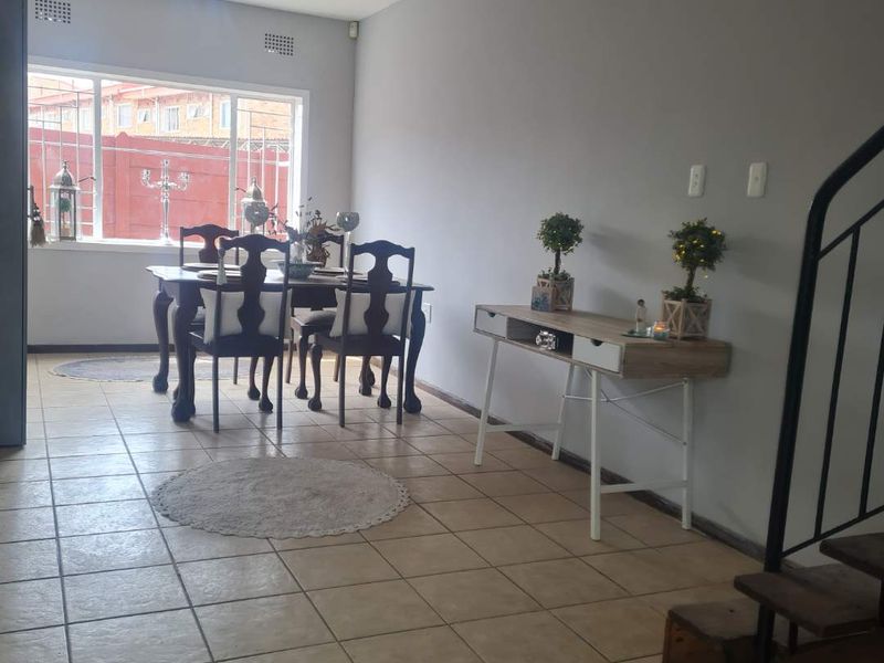 A bright dining area featuring tiled flooring, a large window with security bars, and an adjacent staircase with a metal railing.