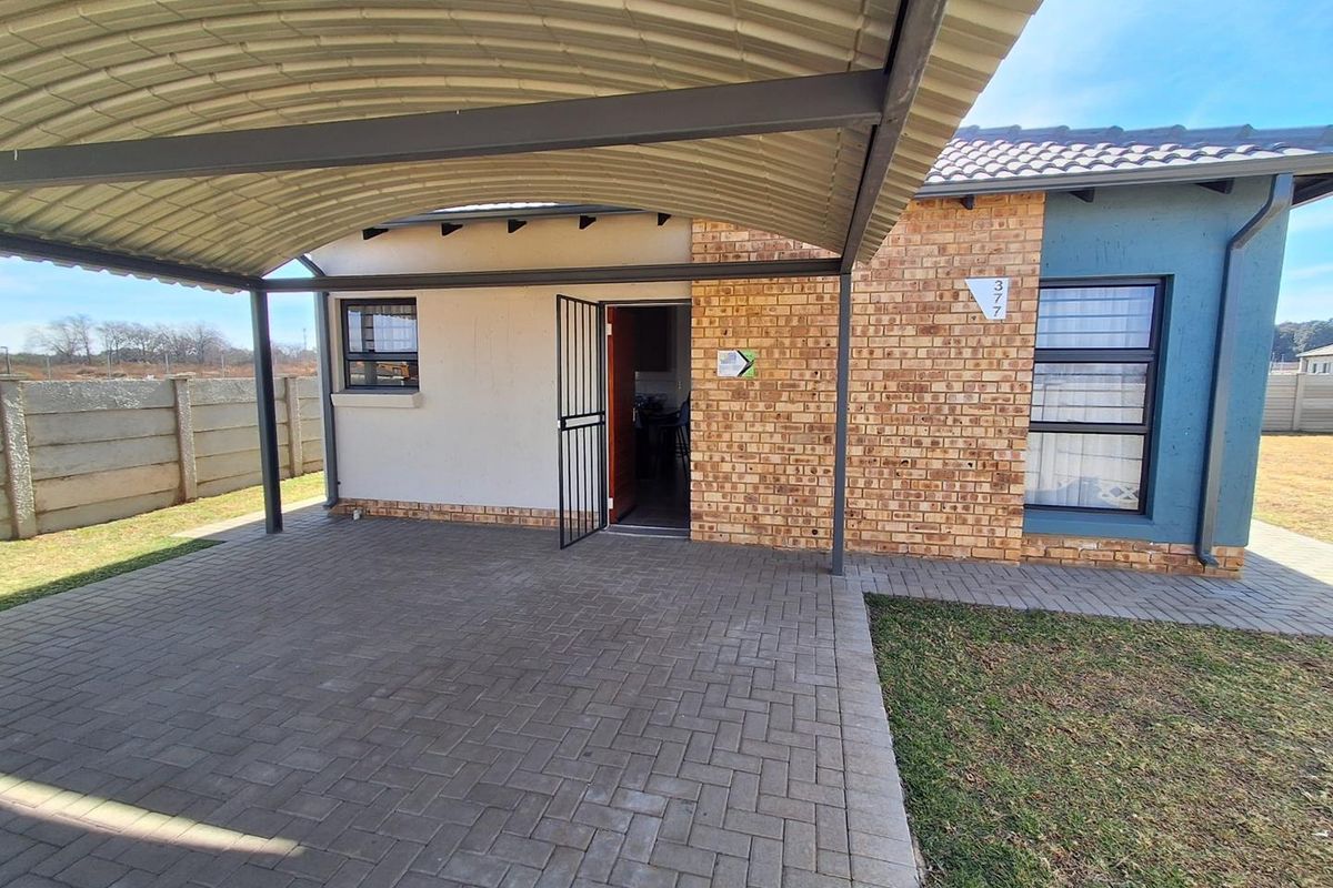 Front exterior view featuring a paved driveway, covered carport, brick and painted facade, and secure entrance gate.