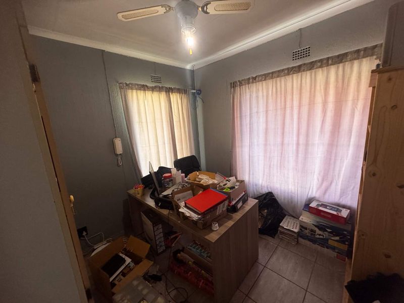 A compact bedroom featuring tiled flooring, a ceiling fan, and dual windows, offering a functional space that could benefit from cosmetic updates.