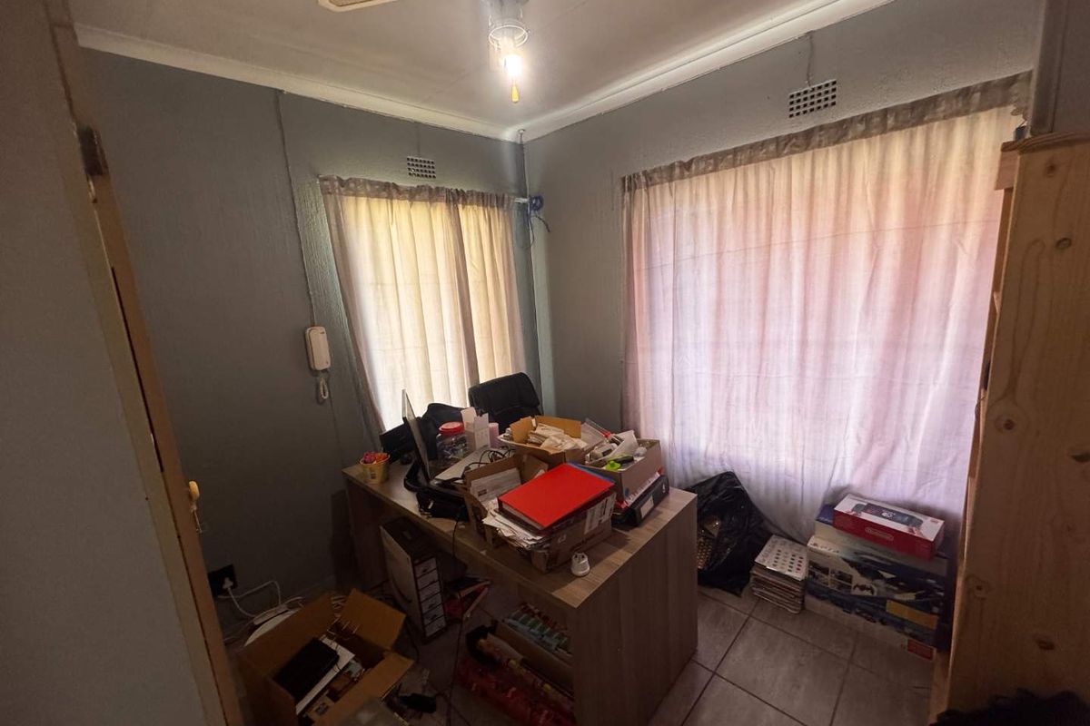 A compact bedroom featuring tiled flooring, a ceiling fan, and dual windows, offering a functional space that could benefit from cosmetic updates.