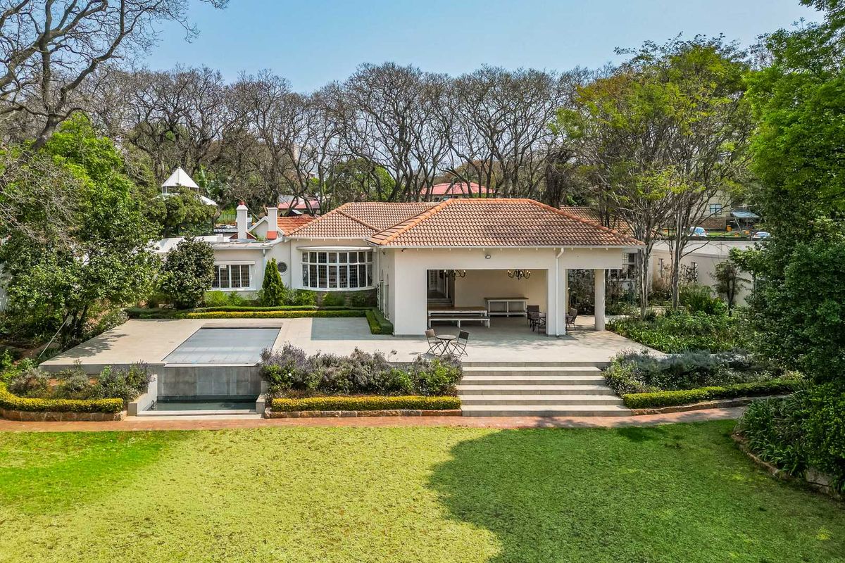 Rear view of the property featuring a covered patio, swimming pool, and expansive landscaped garden with mature trees.