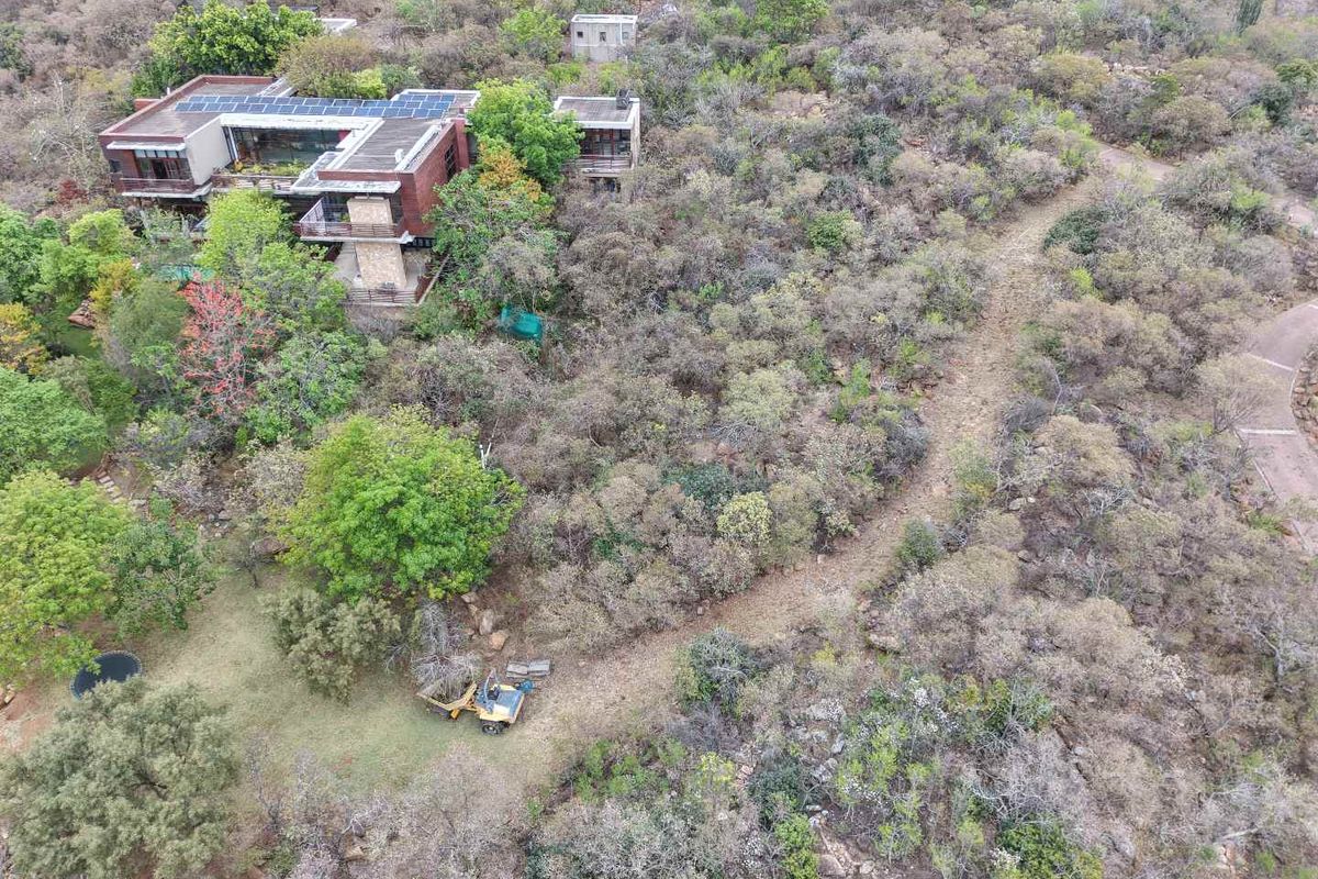 Aerial view of a modern multi-level small holding property featuring stone accents, solar panels, and extensive natural vegetation.
