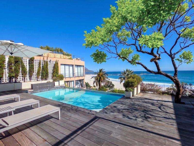An elevated outdoor pool area featuring timber decking and a swimming pool with panoramic ocean and beach views.