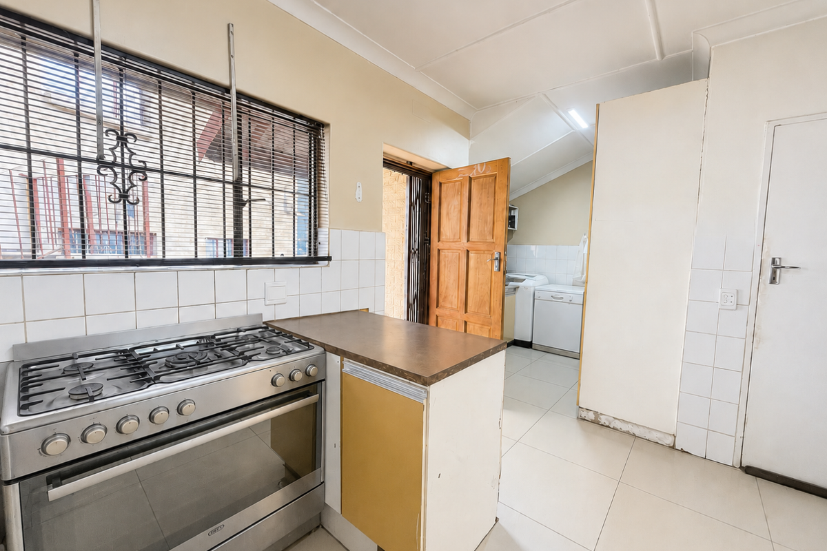 Functional kitchen featuring a gas stove, tiled splashbacks, and tiled flooring, with an adjacent laundry area visible through the doorway.