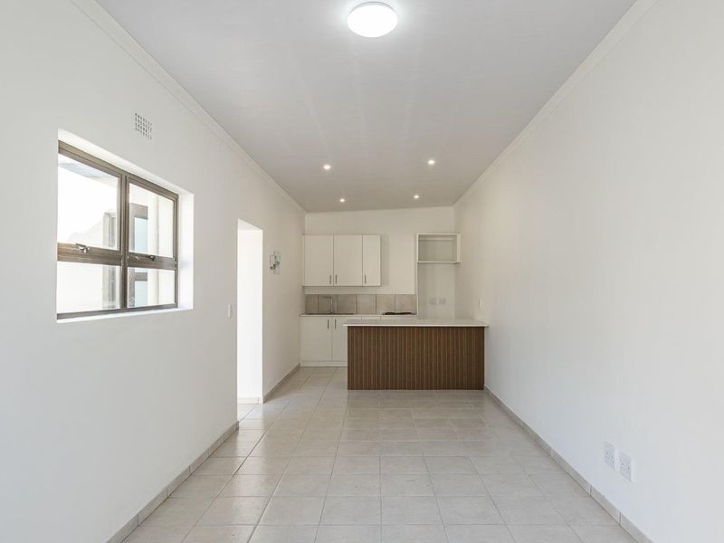 An open-plan kitchen and living area featuring neutral tiled flooring, modern cabinetry, a kitchen island, and recessed lighting in a clean, vacant space.