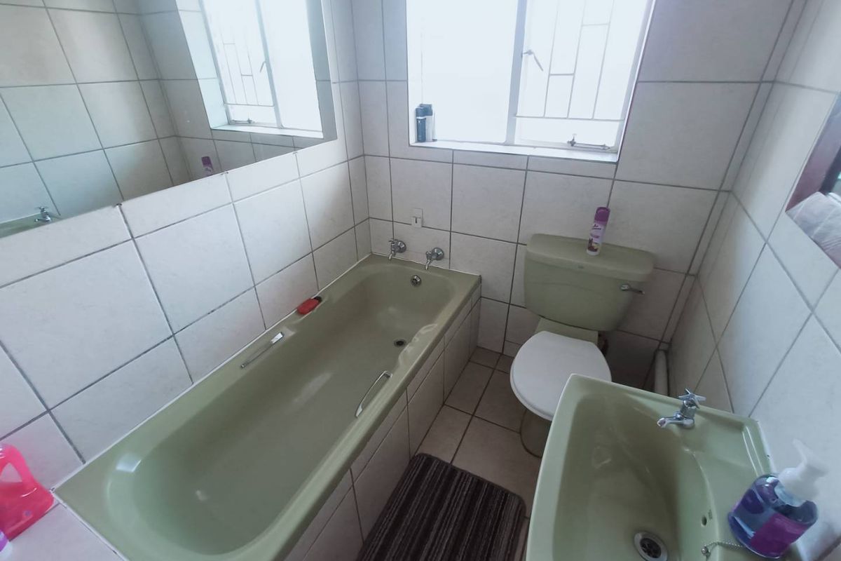 A dated bathroom featuring a vintage green bathtub, matching pedestal basin, and toilet, complemented by full-height wall tiling and a large wall-mounted mirror.