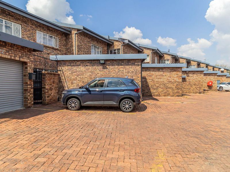 Front exterior view of a townhouse complex featuring face-brick facades, paved driveway access, and individual roller garage doors.