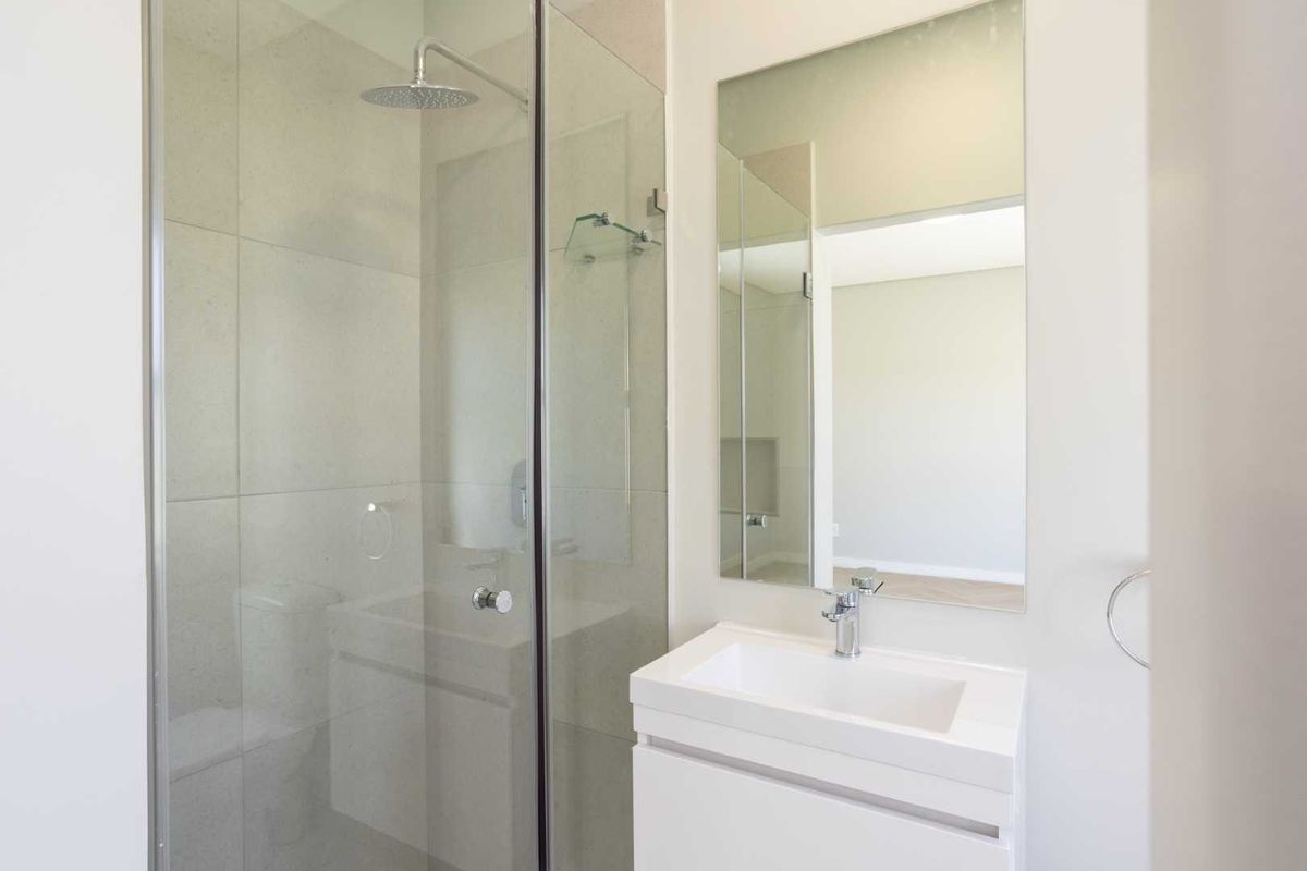 Modern bathroom featuring a glass-enclosed walk-in shower with rainfall showerhead and a sleek wall-mounted vanity with integrated basin and mirror.