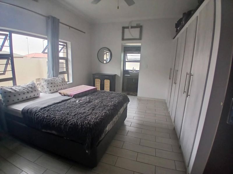 Spacious bedroom featuring built-in cupboards, tiled flooring, and a ceiling fan, with an adjoining en-suite bathroom visible.