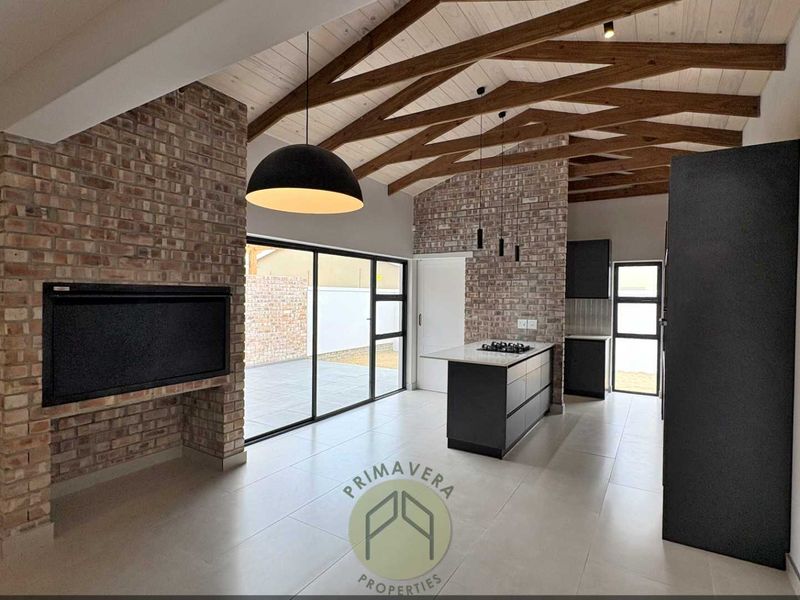Modern open-plan living area featuring exposed timber beams, a brick fireplace, and a sleek kitchen island with a gas hob and sliding door access.