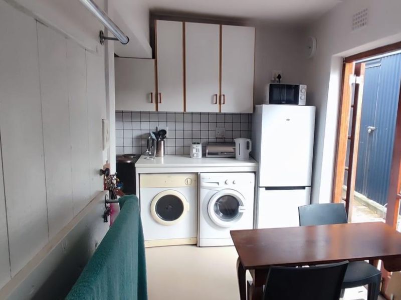 Compact laundry area featuring built-in cabinetry, tiled splashback, and dedicated plumbing connections for laundry appliances, with direct access to the rear exterior.