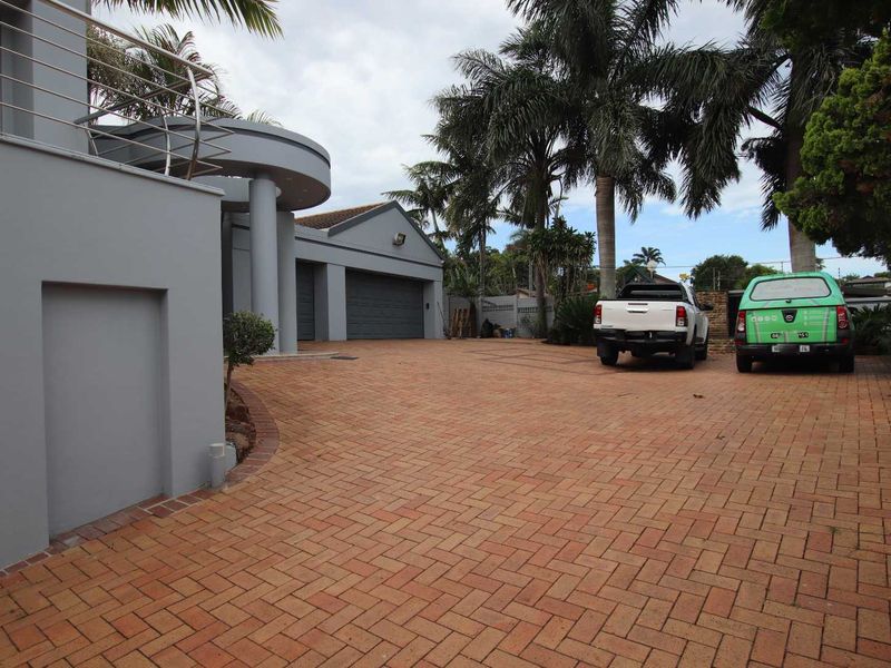 Front exterior view of the property featuring a paved driveway, double garage, and a modern balcony with stainless steel railings.