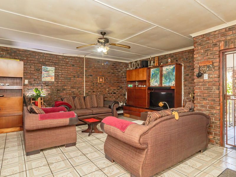 Spacious living room featuring exposed brick walls, tiled flooring, and a ceiling fan, with direct access to an outdoor area through a security gate.