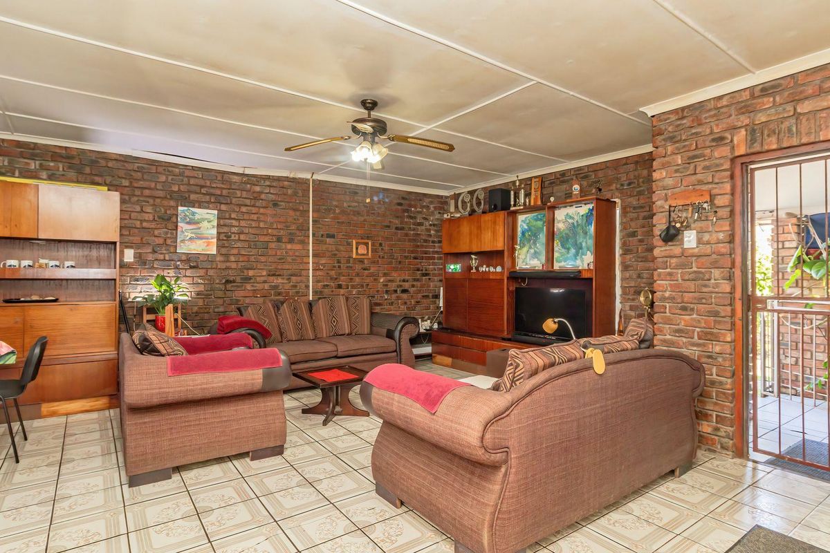 Spacious living room featuring exposed brick walls, tiled flooring, and a ceiling fan, with direct access to an outdoor area through a security gate.