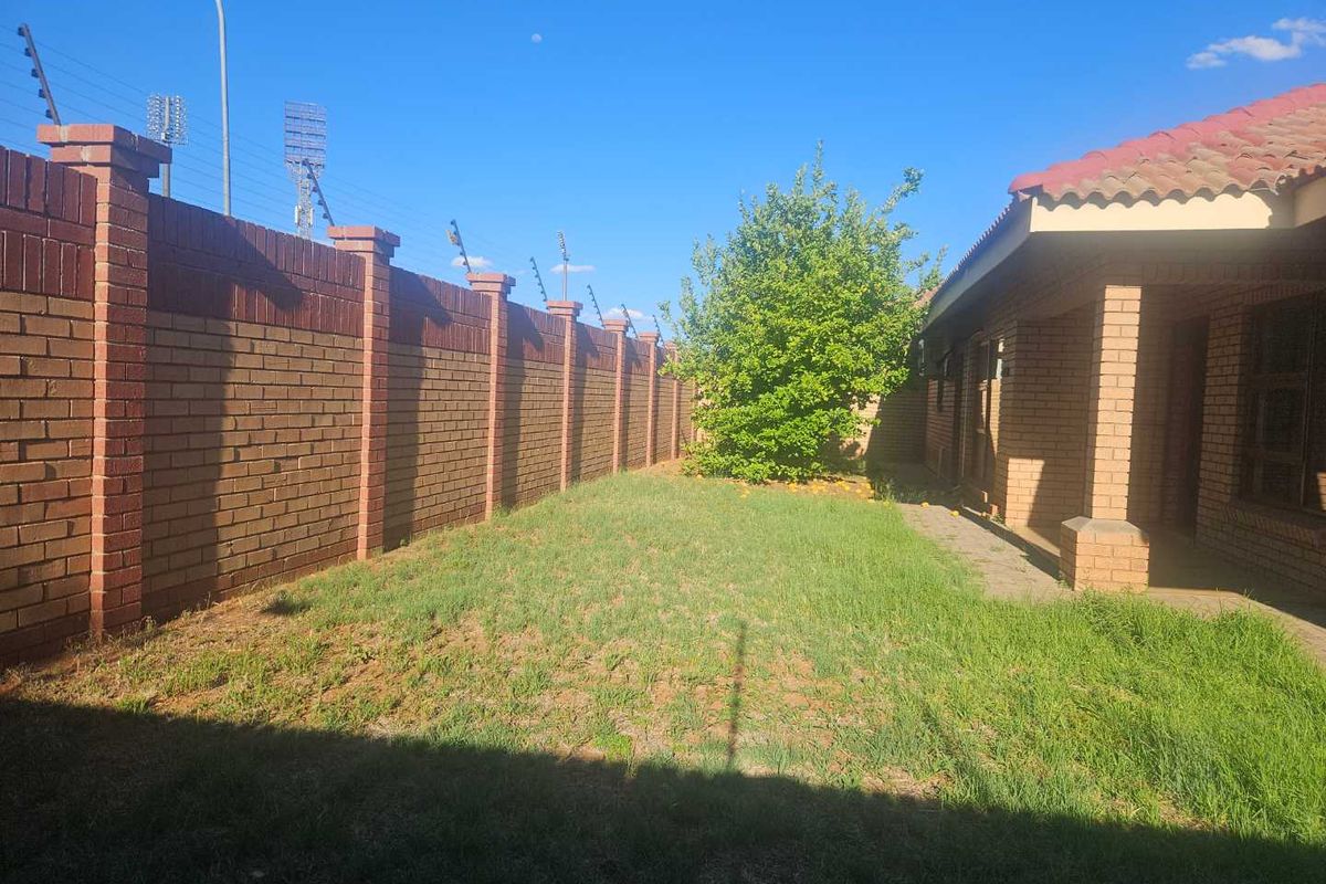 A private rear garden featuring a brick boundary wall with electric fencing, a small lawn area, and a paved walkway along the townhouse exterior.