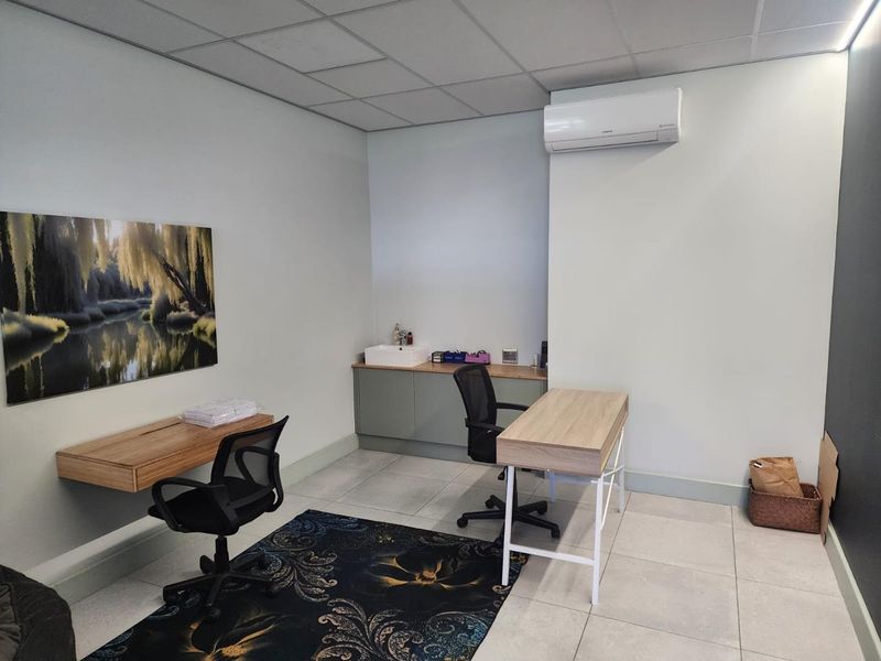A professional office space featuring a suspended ceiling, wall-mounted air conditioning, and a built-in vanity cabinet with a basin.