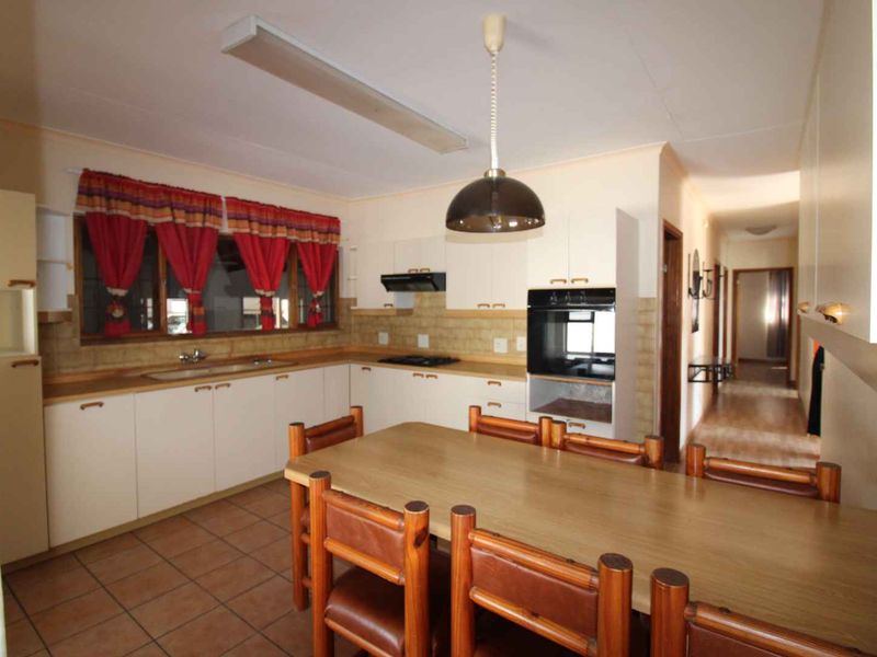 A functional kitchen featuring built-in cabinetry, integrated oven and hob, tiled backsplash, and tiled flooring, with an adjacent hallway leading to other rooms.