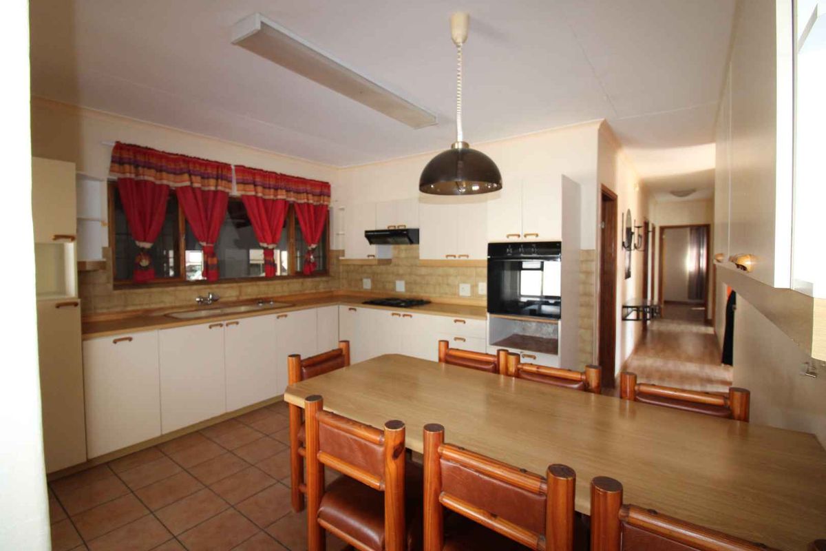 A functional kitchen featuring built-in cabinetry, integrated oven and hob, tiled backsplash, and tiled flooring, with an adjacent hallway leading to other rooms.
