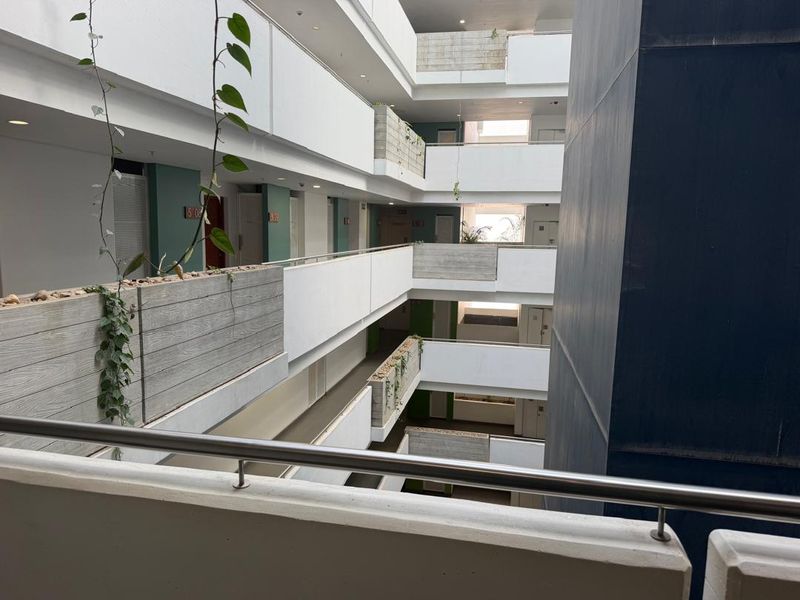 An open-air apartment building atrium featuring multi-level walkways with stainless steel railings and integrated concrete planter boxes.