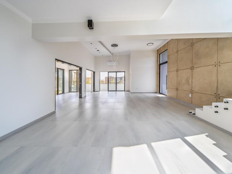 Spacious open-plan living area featuring large format floor tiles, a modern feature wall, recessed lighting, and seamless access to outdoor spaces.