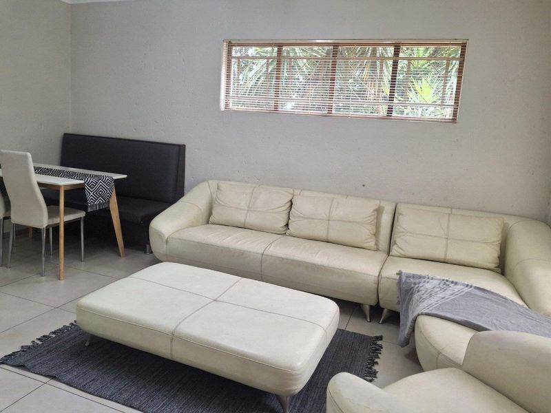 A living room area featuring neutral tiled flooring and a horizontal window with fitted blinds, providing a functional and well-lit space.