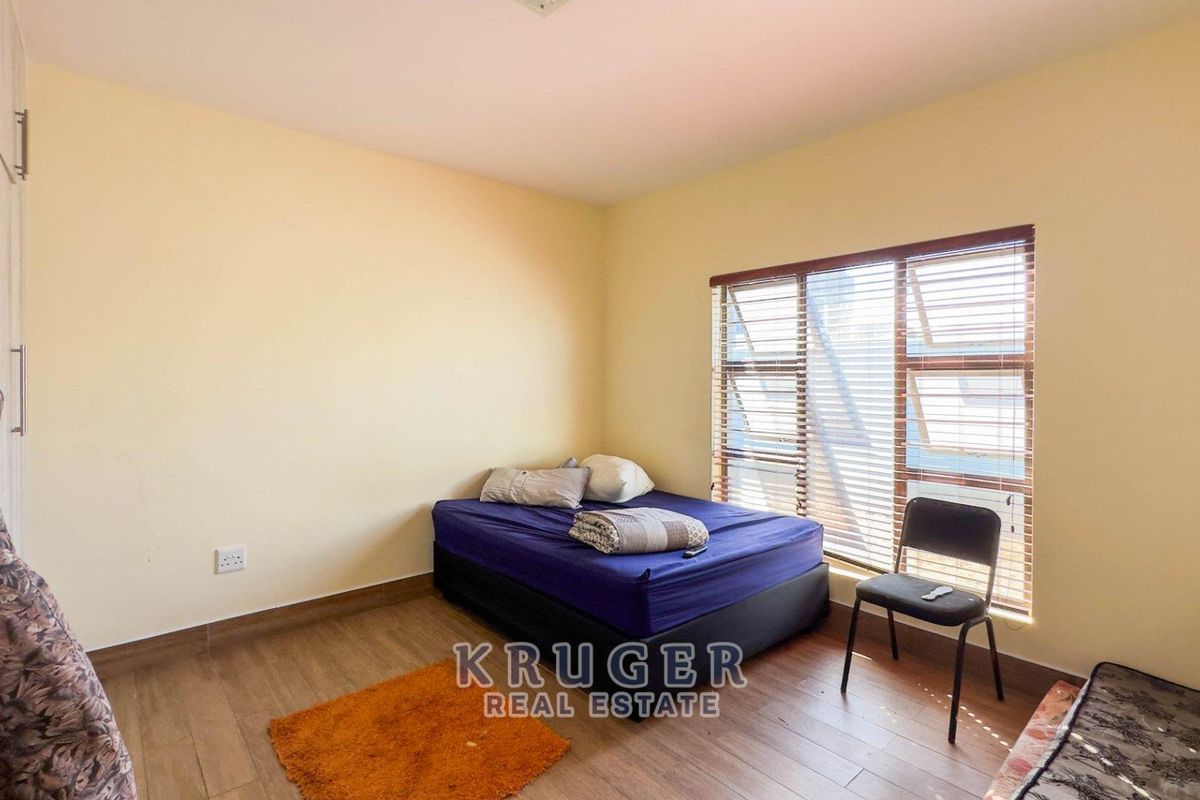 A bedroom featuring wood-look flooring, built-in cupboards, and large windows fitted with horizontal blinds.