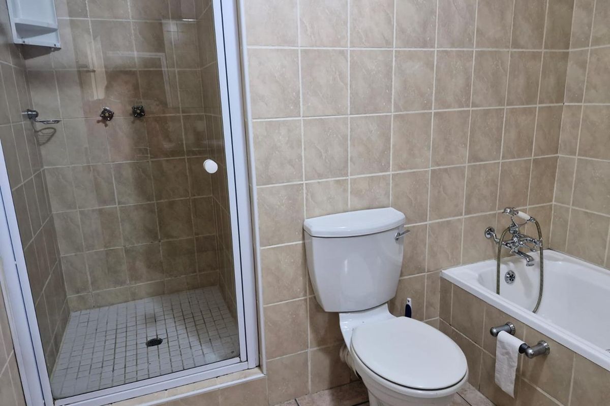 A functional bathroom featuring a separate shower enclosure, a standard toilet, and a bathtub with a handheld shower mixer, finished with neutral wall tiles.