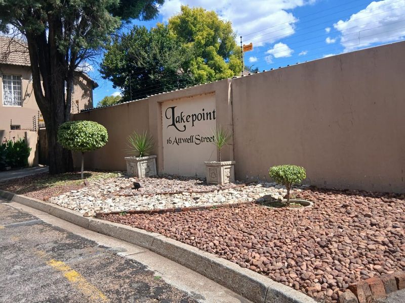 Street-level view of the Lakepoint apartment complex entrance, featuring a perimeter boundary wall with signage and landscaped rock garden beds.