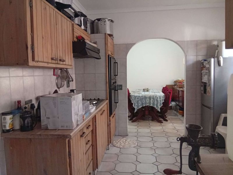 A dated kitchen featuring wooden cabinetry, tiled backsplash, and a built-in oven, with an arched opening leading to the adjacent dining area.