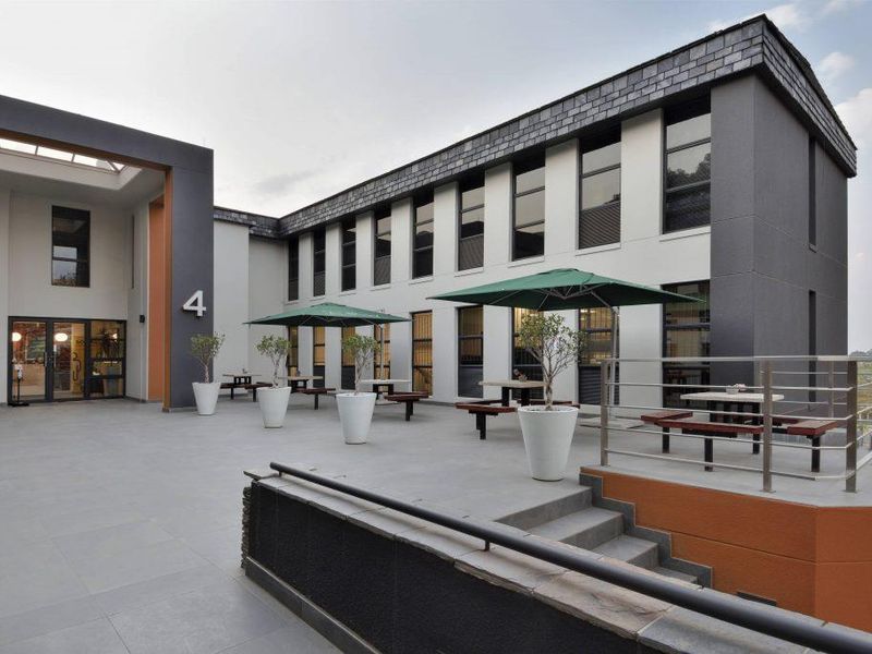A modern, well-maintained outdoor patio area featuring tiled flooring, stainless steel railings, and direct access to the office building facade.