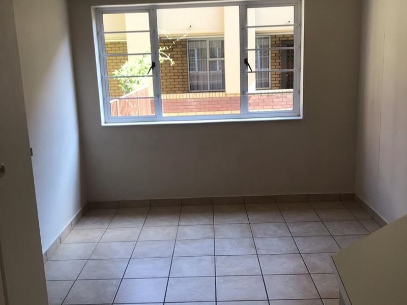 A clean, empty bedroom featuring neutral tiled flooring and a window with security bars, providing a blank canvas for personalization.