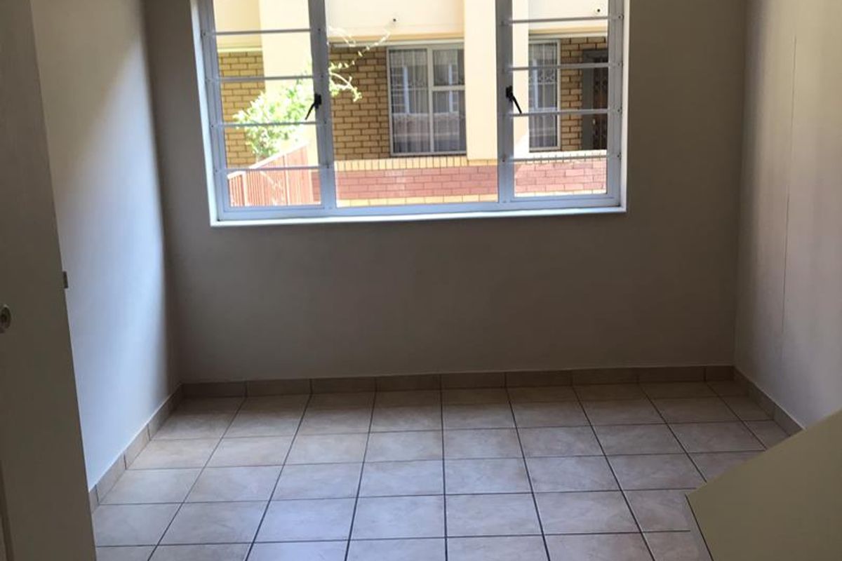 A clean, empty bedroom featuring neutral tiled flooring and a window with security bars, providing a blank canvas for personalization.