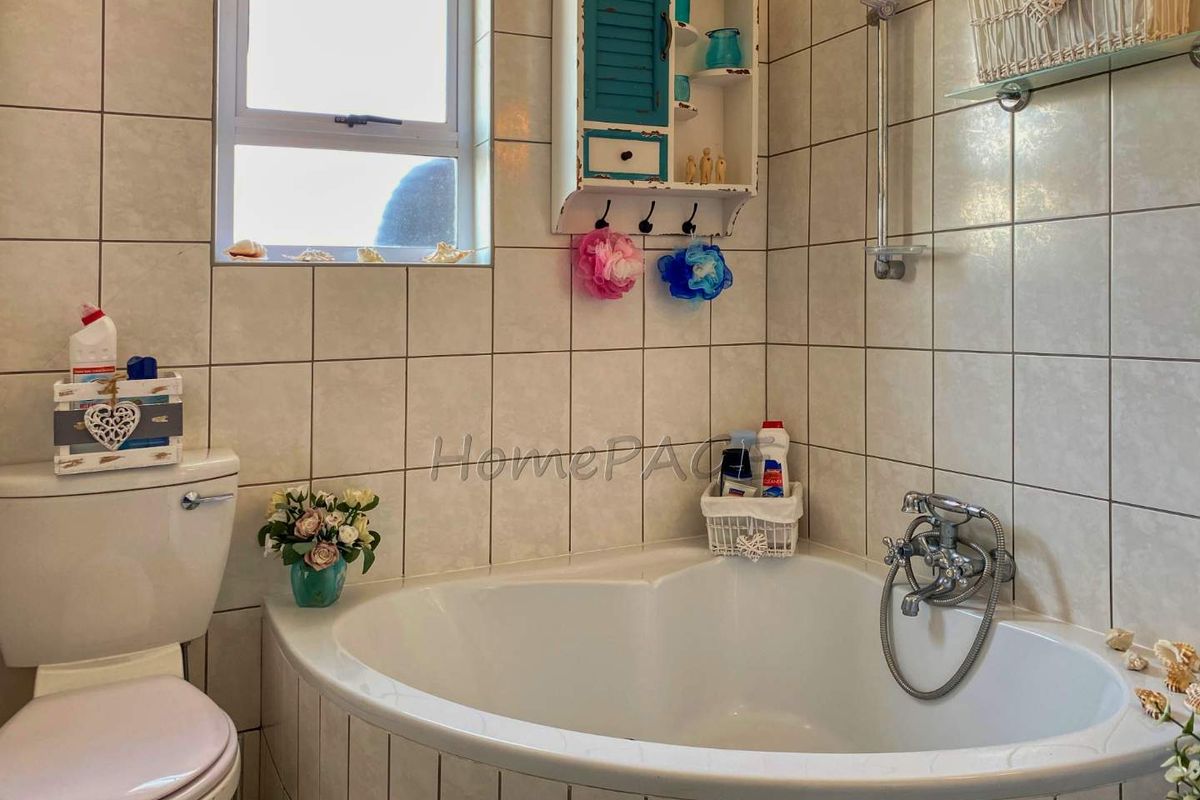 A bathroom featuring a corner bathtub, a standard toilet, and tiled walls with a window for natural light.