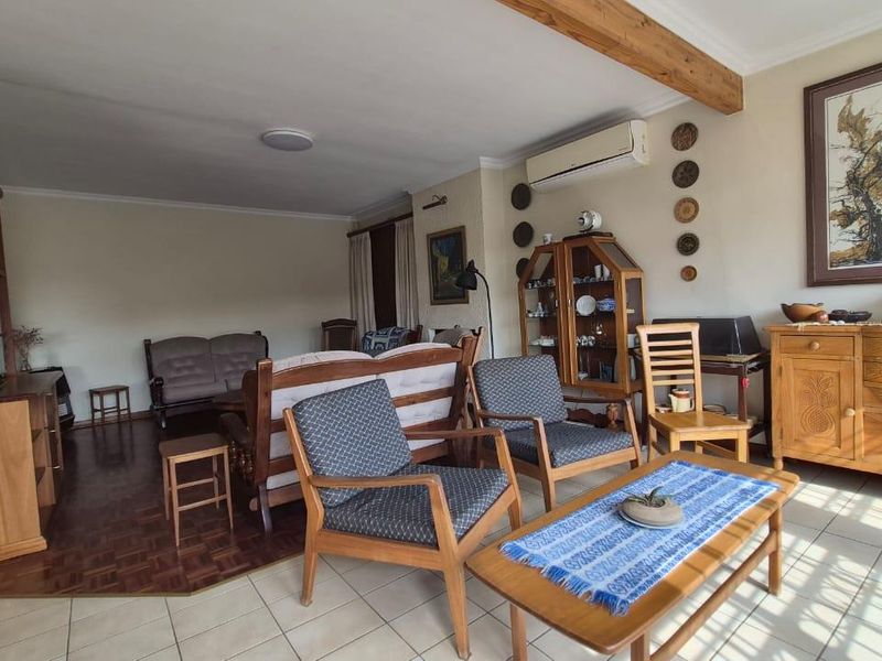 A spacious living area featuring a combination of parquet and ceramic tile flooring, an exposed timber ceiling beam, and a wall-mounted air conditioning unit.