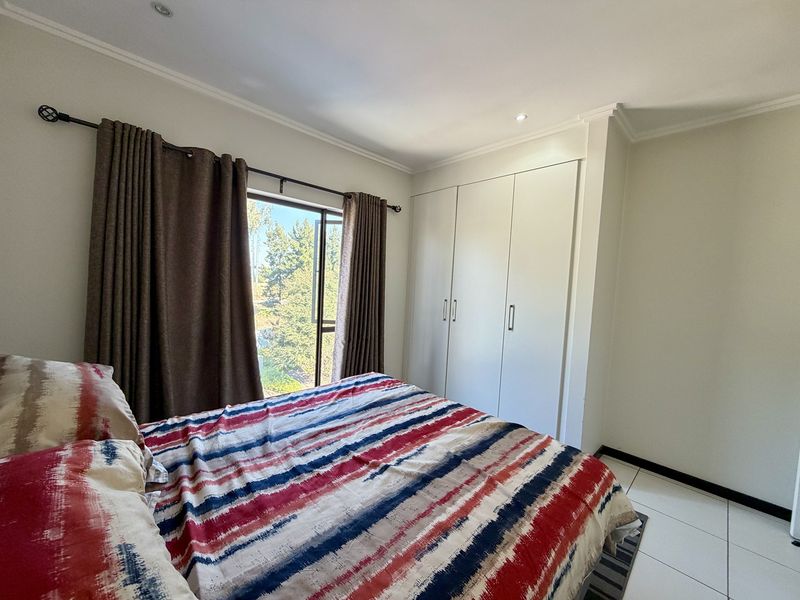 A well-maintained bedroom featuring built-in cupboards, tiled flooring, and recessed downlights, offering a clean and functional living space.