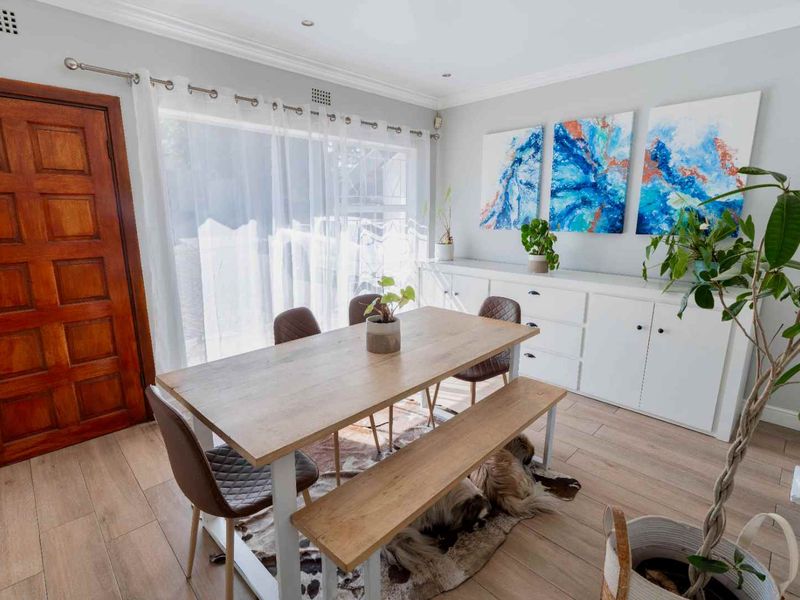 A bright dining room featuring light wood-look laminate flooring, built-in white cabinetry, and a solid timber entrance door.