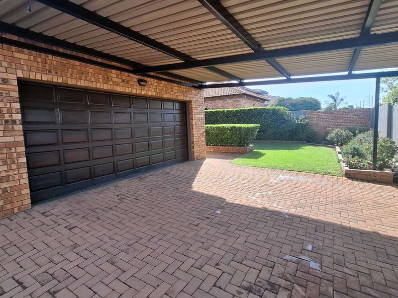 A well-maintained exterior view featuring a brick garage with a sectional door, a covered carport, and a paved driveway leading to a landscaped garden.
