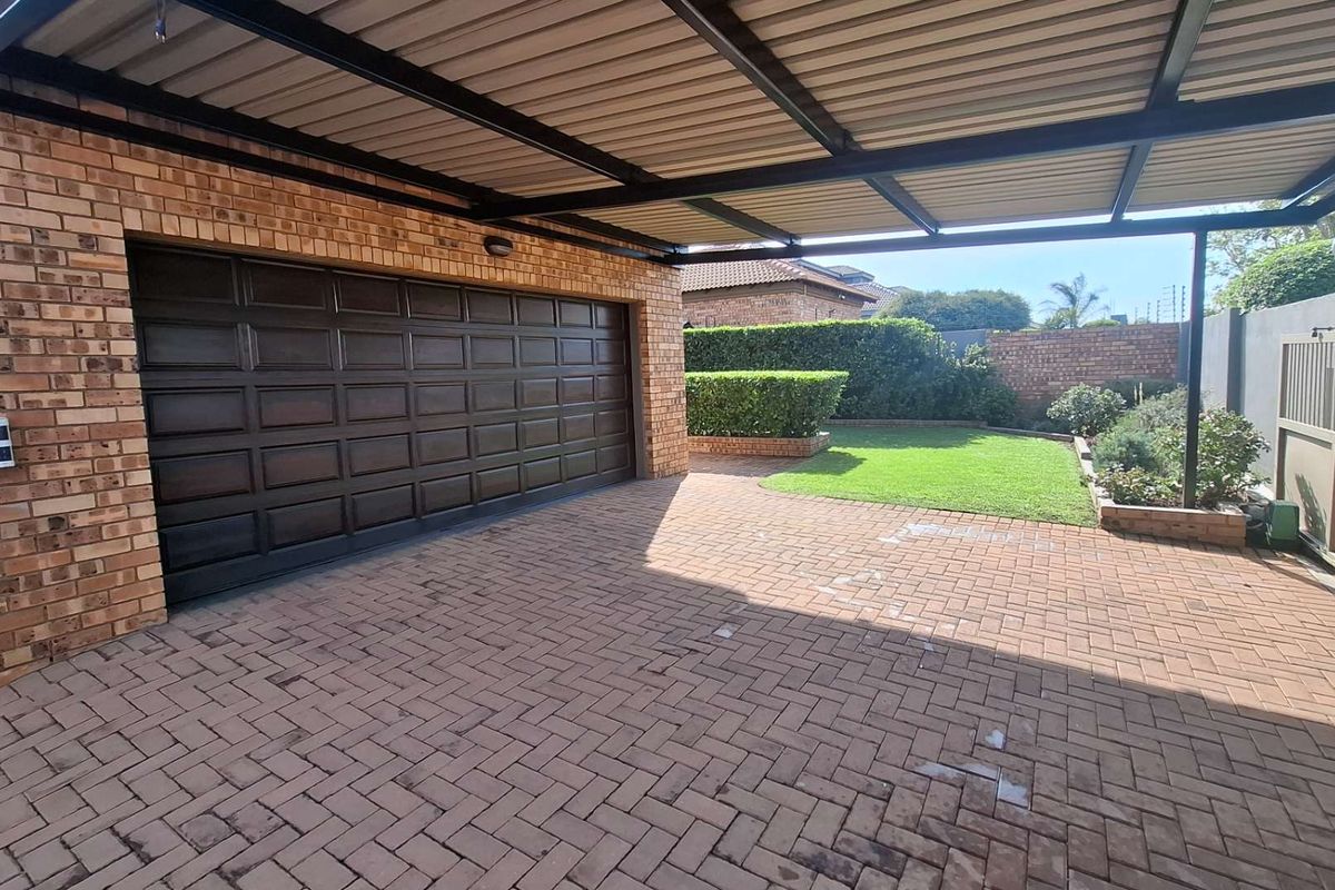 A well-maintained exterior view featuring a brick garage with a sectional door, a covered carport, and a paved driveway leading to a landscaped garden.