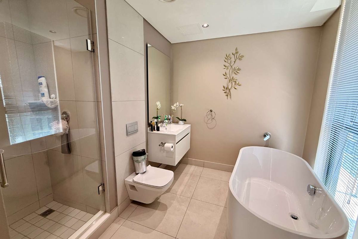 Modern bathroom featuring a wall-mounted vanity, a glass-enclosed walk-in shower, and a contemporary freestanding bathtub with neutral floor-to-ceiling tiling.