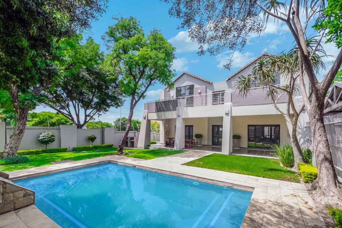 Rear view of the apartment featuring a private swimming pool, paved patio area, landscaped garden, and an upper-level balcony.