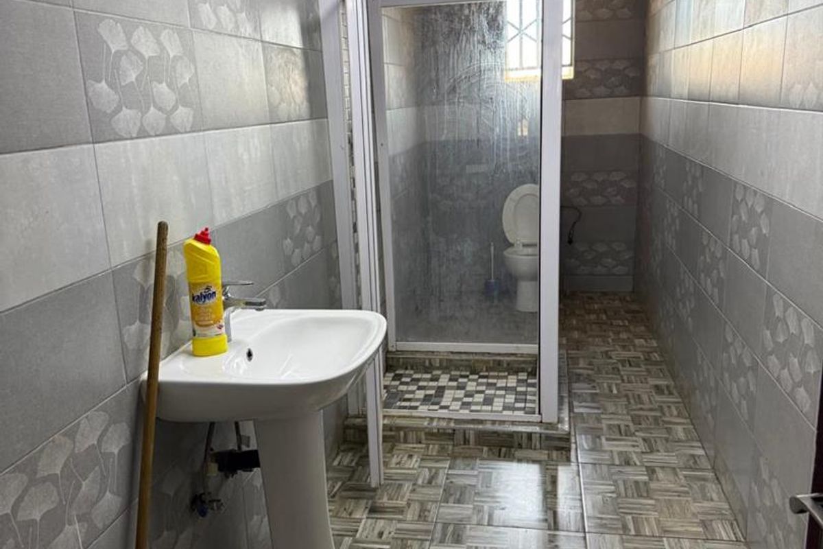 A functional bathroom featuring a pedestal basin, a separate shower enclosure, and a toilet, finished with patterned wall and floor tiling.