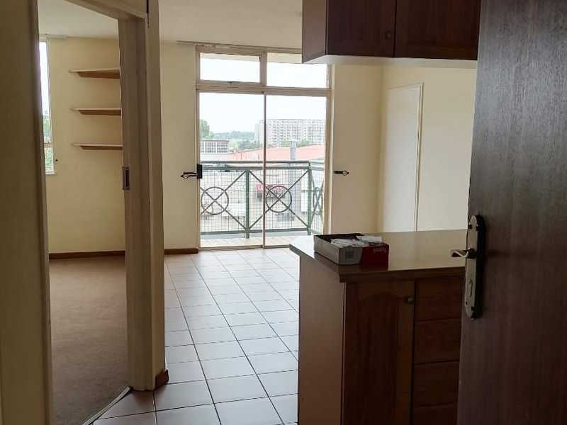 An open-plan living area featuring tiled floors, built-in cabinetry, and a sliding glass door leading to a balcony with metal railings.