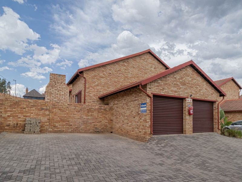 Front exterior view of a townhouse featuring a double garage with roller doors, brick facade, and a paved driveway.