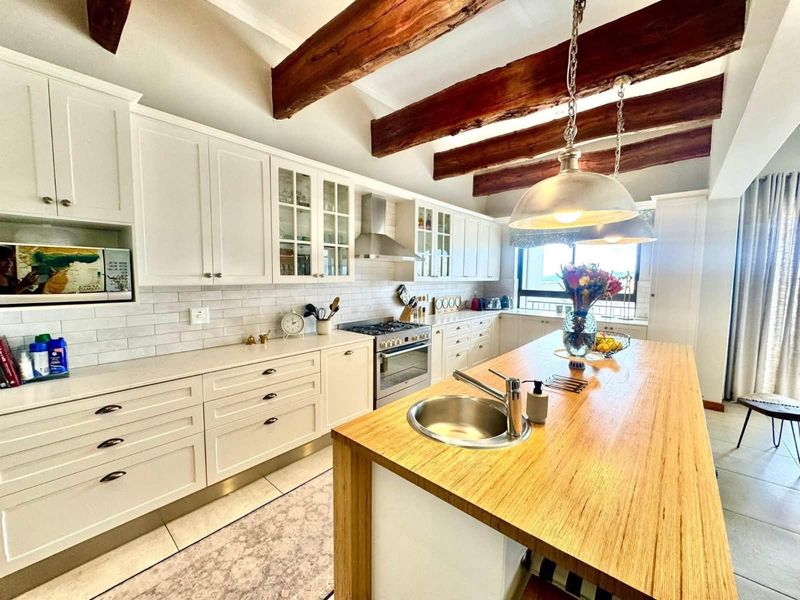 A well-appointed kitchen featuring white shaker cabinetry, subway tile backsplash, a central island with a butcher block countertop, and rustic exposed timber ceiling beams.
